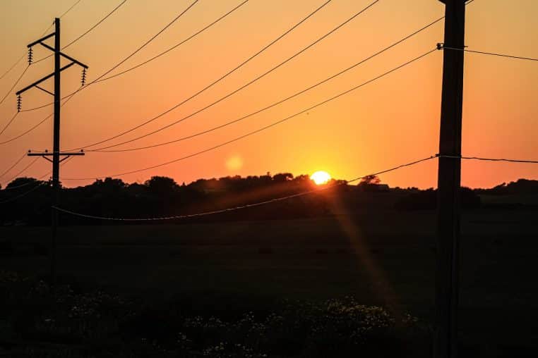 Pylônes électriques sur ciel orangé au coucher du soleil.