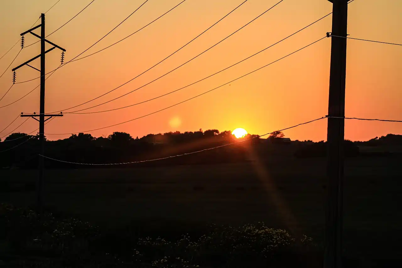 Pylônes électriques sur ciel orangé au coucher du soleil.