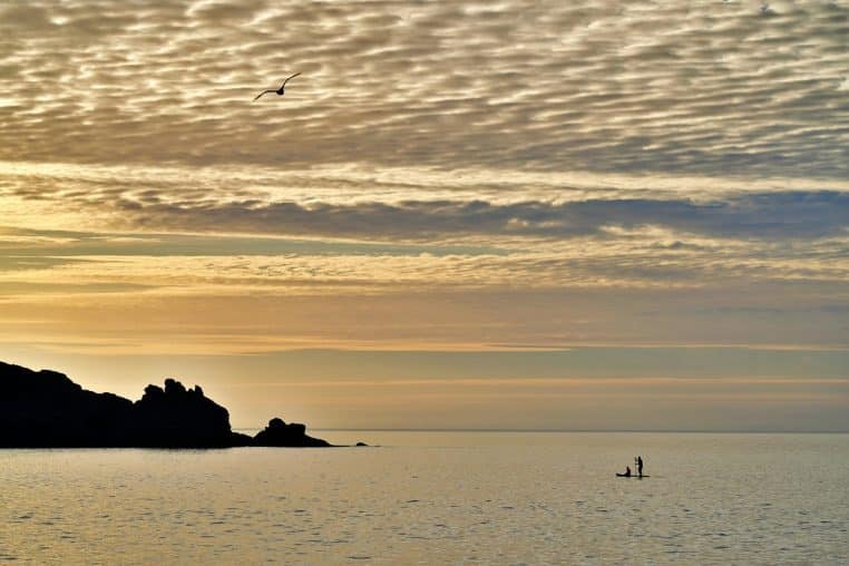 Coucher de soleil orangé sur l’océan, ciel voilé et vagues calmes.