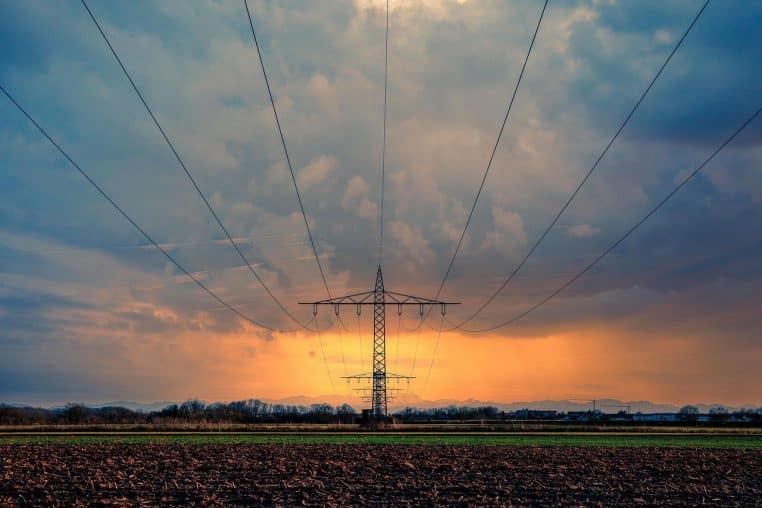 Lignes électriques traversant un ciel nuageux au coucher du soleil.