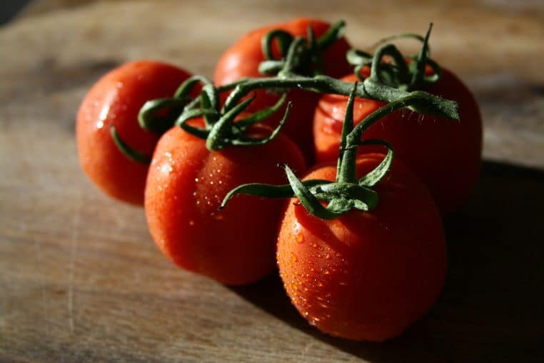 A group of four tomatoes sitting on top of a wooden cutting board
