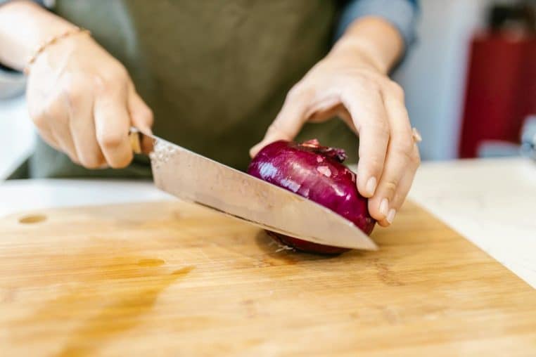 Close-up of hands cutting a red onion on a wooden board indoors.