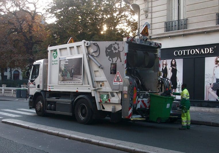 Agent de collecte et camion poubelle devant un kiosque parisien lors d’une tournée en fin de journée, benne prête à charger.