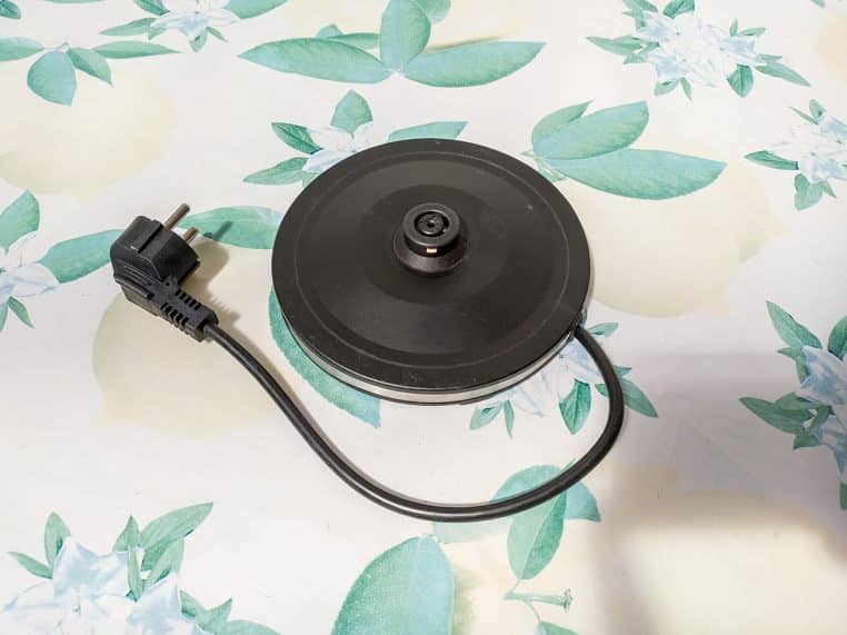 Bouilloire électrique moderne en extérieur sur table, vue latérale avec bec verseur et poignée, image nette en format paysage.