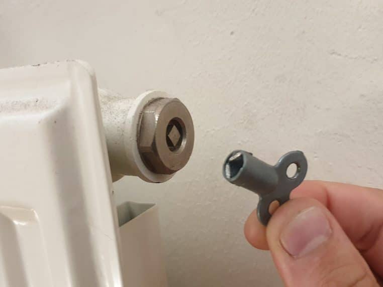 Gros plan d’une clé de purge insérée dans la vis d’un radiateur domestique, prête à évacuer l’air qui empêche une chauffe homogène.
