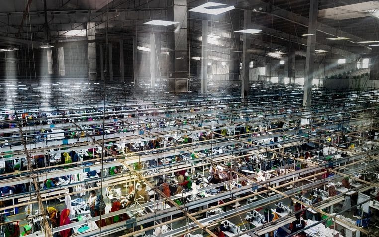 Vue large d’un complexe d’usines de vêtements au Bangladesh, bâtiments modernes et alignements industriels sous ciel clair.
