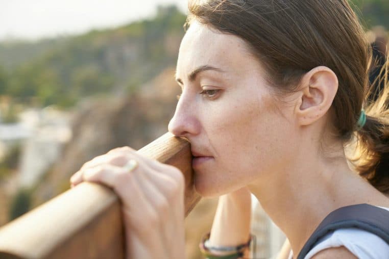 A thoughtful woman leans on a railing, lost in deep contemplation outdoors.