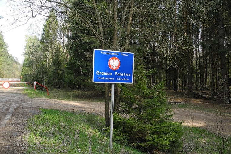 Deux poteaux frontaliers rouge-blanc et rouge-vert alignés en lisière