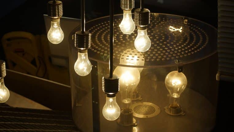 Image horizontale d’une ampoule à filament moderne allumée, verre transparent et lueur ambrée homogène, fond doux.