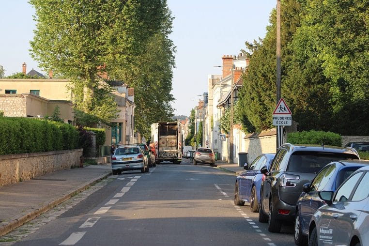 Camion de collecte des déchets circulant dans une rue de Fontainebleau, façades claires et stationnement résidentiel.