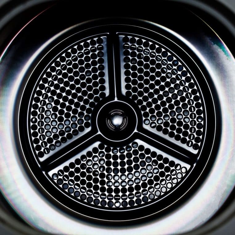 Gros plan sur le hublot et le tambour d’un lave-linge frontal, métal et verre, éclairage doux.