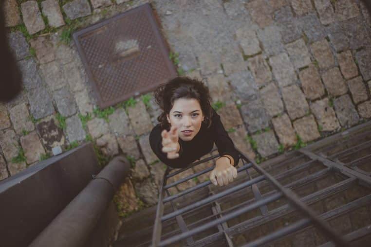 A woman reaching upwards while climbing a ladder on a stone pathway, captured from above.