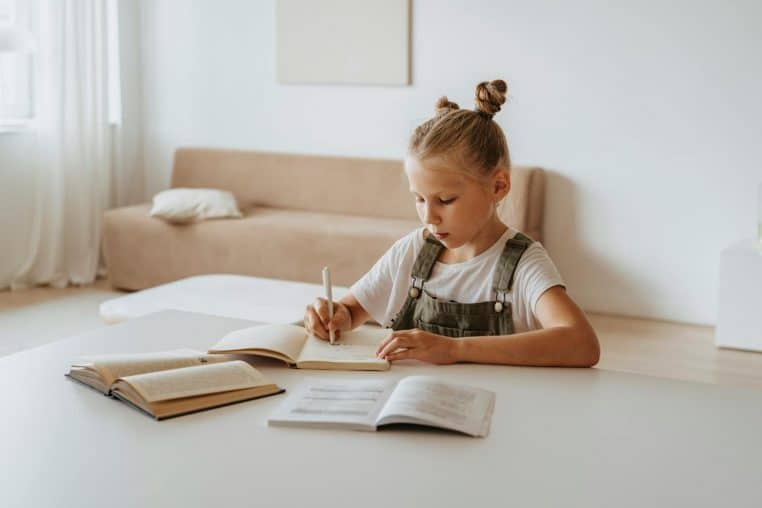 A young girl in a peaceful home setting focused on studying and writing in notebooks.