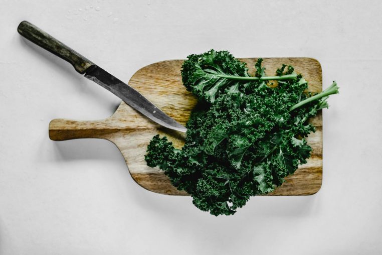 Top view of fresh kale on a wooden chopping board with knife, promoting healthy eating and food preparation.