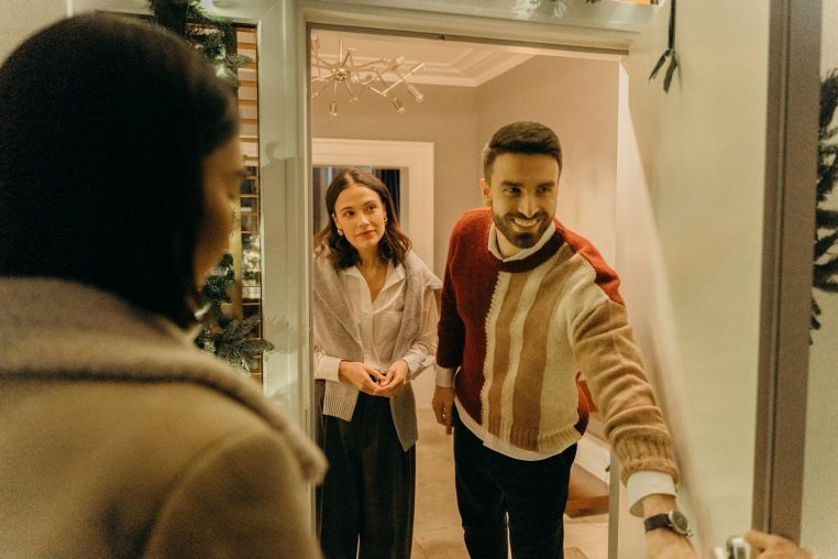 A couple greeting a guest at their doorway, capturing the warmth of a home during the holiday season.