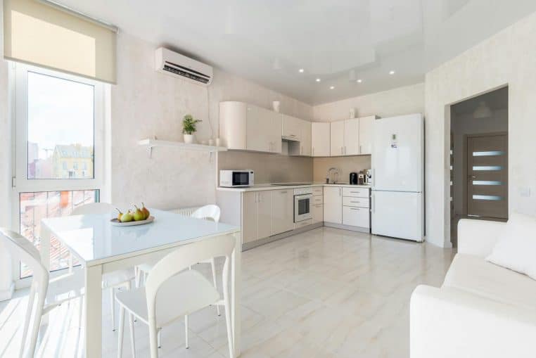 Spacious contemporary kitchen interior featuring white furniture, appliances, and natural light.