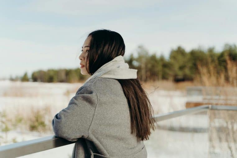 A woman in a warm coat looks out over a snowy landscape, enjoying the serene winter atmosphere.