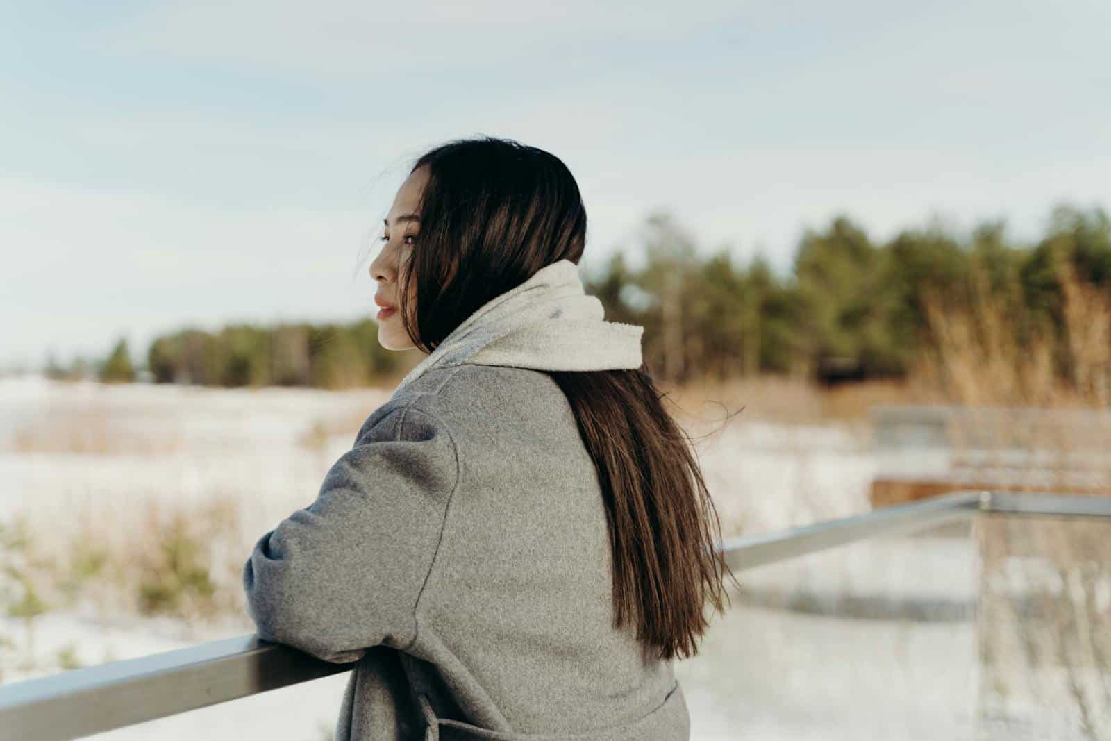 A woman in a warm coat looks out over a snowy landscape, enjoying the serene winter atmosphere.
