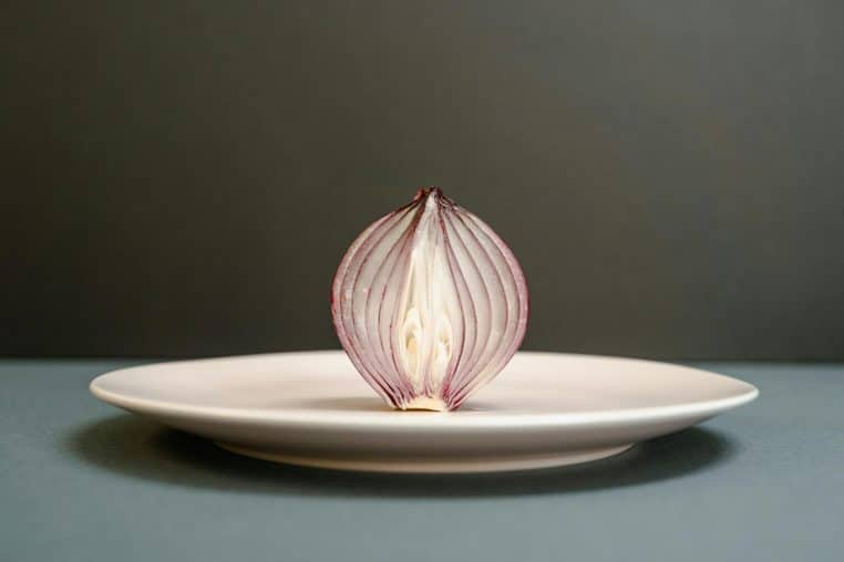 A half-sliced red onion creatively displayed on a white plate against a dark backdrop, highlighting detailed textures.