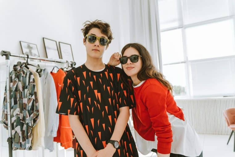 Two teens in stylish outfits and sunglasses posing in a bright room with modern decor.