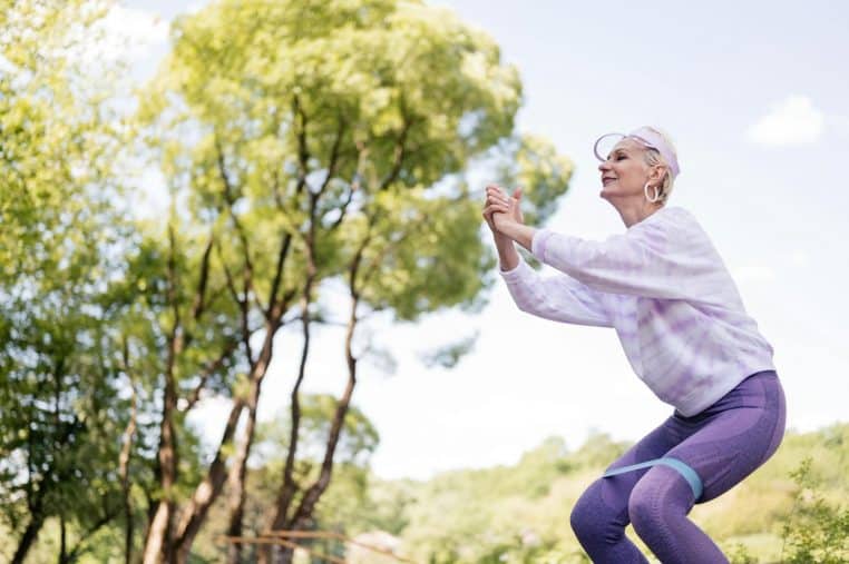 A senior woman exercises in a park with a resistance band, embracing a healthy lifestyle.