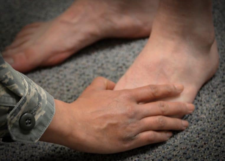 Main du thérapeute palpant l’articulation du pied d’un patient durant une évaluation clinique.