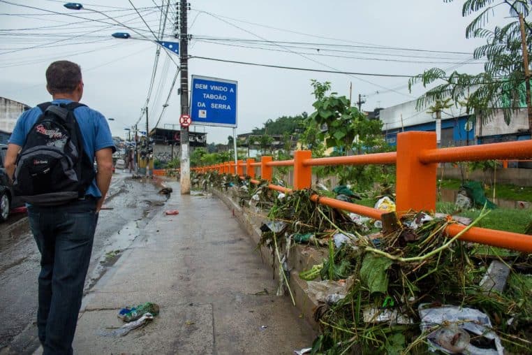 Panneau « Bem-vindo a Taboão da Serra » le long d’un pont, végétaux et débris après pluie, réseau électrique en arrière-plan.