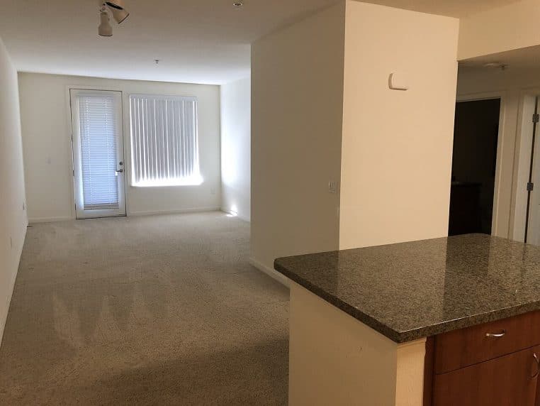 Intérieur d’un salon d’appartement vide et lumineux avec baie vitrée et comptoir, photographié en paysage.