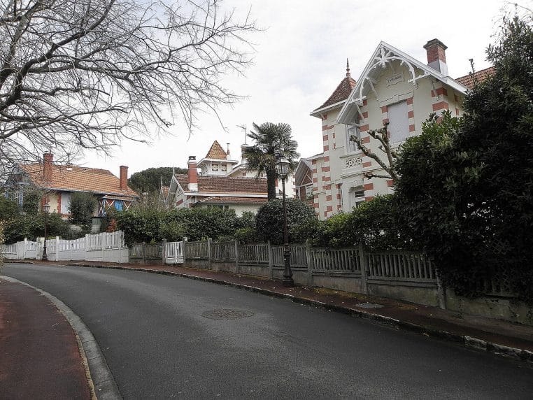 Alignement de villas anciennes à Arcachon, vues depuis la rue, végétation et ciel clair en arrière-plan.