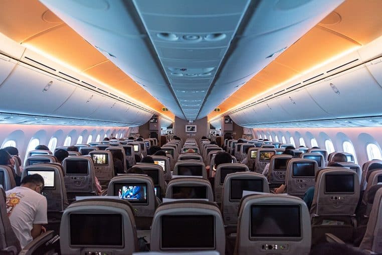 Vue grand-angle d’une cabine économique moderne, passagers assis, coffres à bagages fermés et éclairage chaleureux orangé.