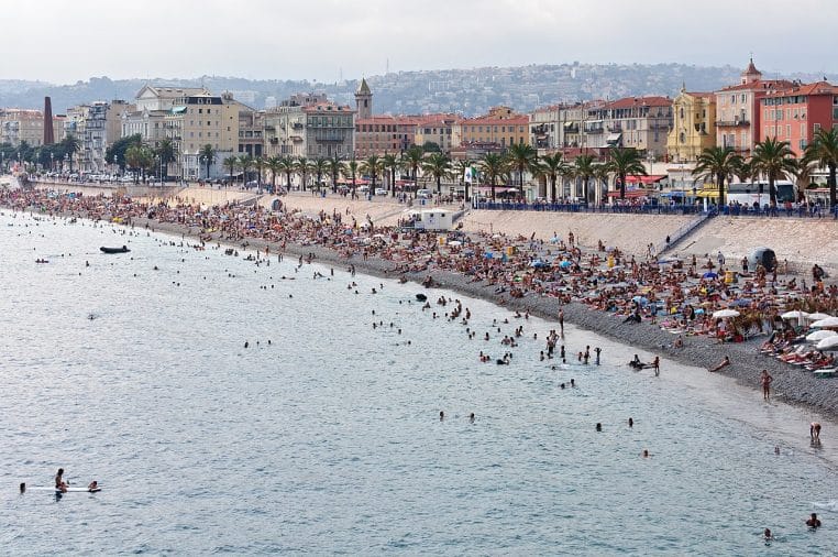 Vue panoramique de la Baie des Anges à Nice avec plage, baigneurs et front de mer sous un ciel d’été légèrement voilé