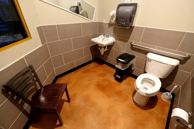 Salle de bains de restaurant, brosse de WC et distributeurs visibles.