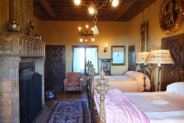 Chambre historique avec tête de lit sculptée et deux lampes de chevet allumées.