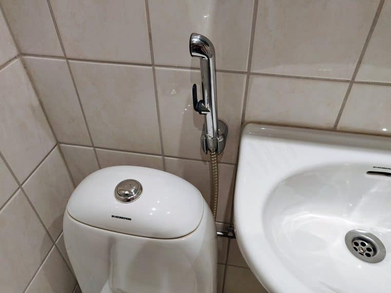 Douchette d’hygiène inox montée près d’un WC dans une salle de bains d’hôtel