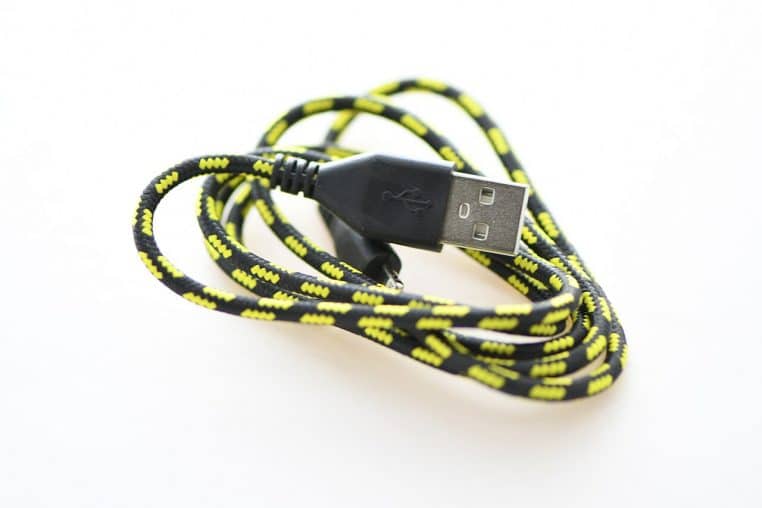 Gros plan d’un chargeur USB noir posé sur une table, câble branché, illustrant les accessoires électriques du quotidien.