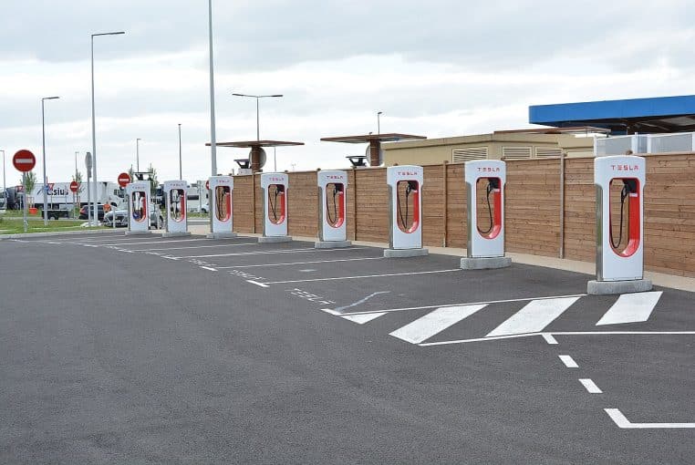 Station Tesla Supercharger sur l’aire du Bourbonnais, autoroute A79 ; rangée de bornes disponibles sous ciel dégagé, parkings matérialisés.