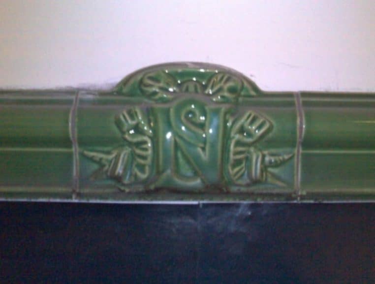 Détail horizontal d’une frise en céramique style Nord-Sud montrant vagues et encadrements, teintes brunes et vertes.