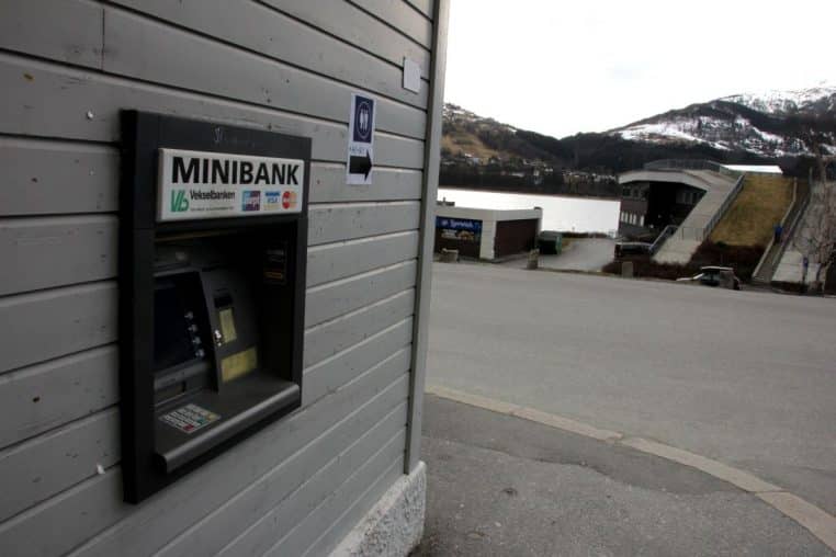 Distributeur encastré sur une façade avec vue sur la rue et le paysage, clavier et fente de carte nettement visibles.
