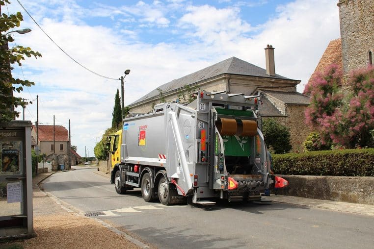 Camion poubelle à l’arrêt devant des habitations, collecte d’ordures en journée dans une commune d’Île-de-France, benne levée.