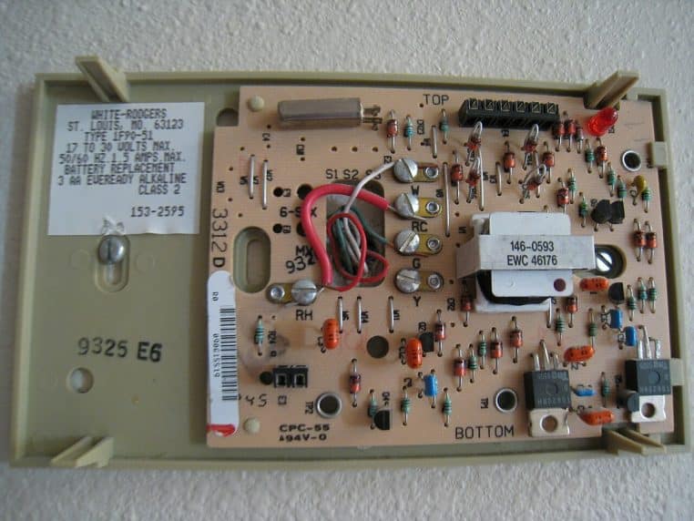 Arrière d’un thermostat numérique mural, carte électronique apparente et borniers repérés.