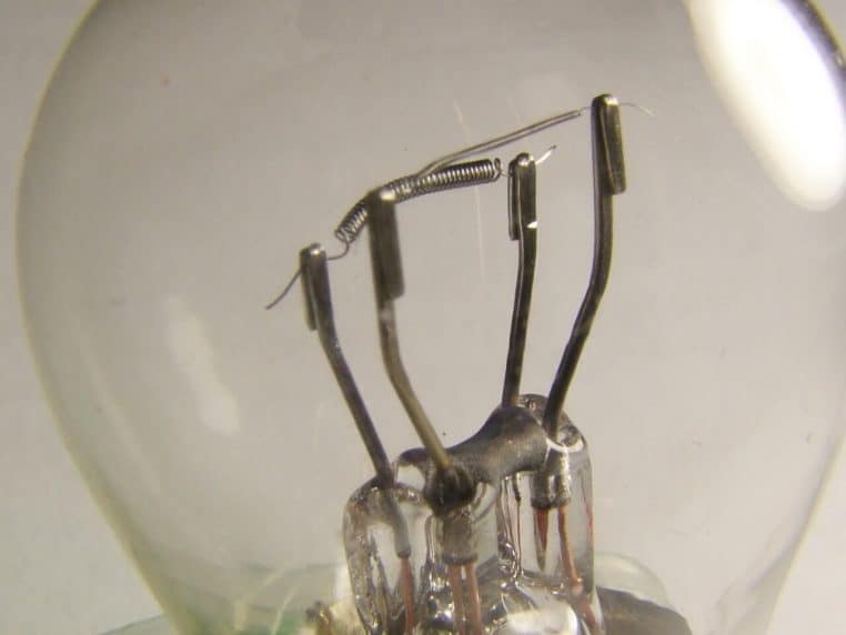 Vue horizontale rapprochée d’une ampoule à double filament, lumière chaude et reflets métalliques nets, sur fond sombre.