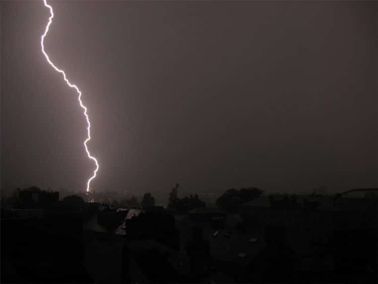 Foudre frappant l’horizon nocturne de Nantes, ciel uniformément sombre et silhouettes de toits au premier plan.