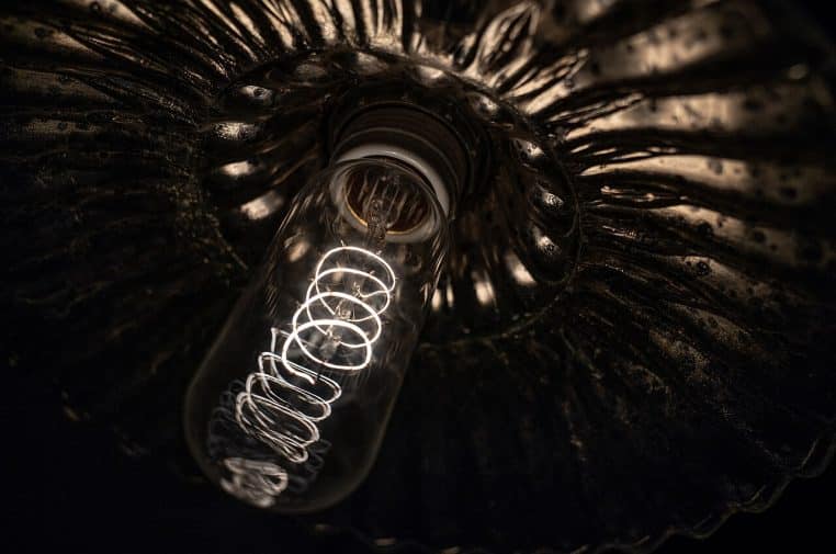 Photo horizontale d’une ampoule Edison d’inspiration vintage, filament apparent et teinte ambrée, sur fond neutre légèrement sombre.