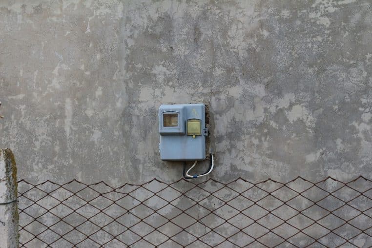 Deux boîtiers de compteurs électriques colorés (jaune et orange) dans une niche extérieure, décorés de plantes »