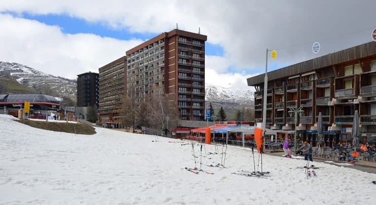 Vue du front de neige de la station du Corbier avec peu de neige au sol, bâtiments et pentes herbeuses visibles en arrière-plan.