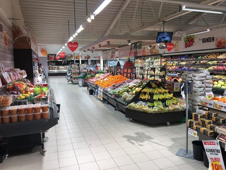 Vue plongeante sur l’allée des fruits et légumes dans un supermarché.