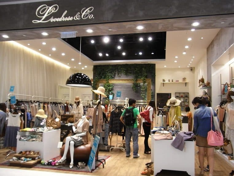 Intérieur de boutique de vêtements avec portants et présentoirs, perspective large en format horizontal, ambiance lumineuse et contemporaine.