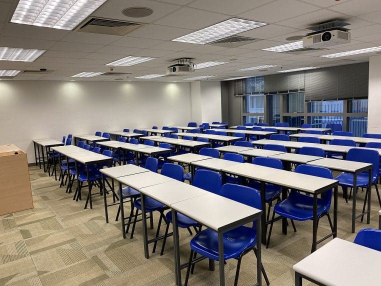 Salle de cours lumineuse à l’Université métropolitaine de Hong Kong, tables alignées et matériel prêt pour un cours magistral.