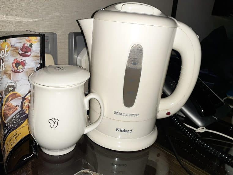 Bouilloire électrique blanche et tasse posées dans une chambre d’hôtel, illustrant un usage simple et quotidien.