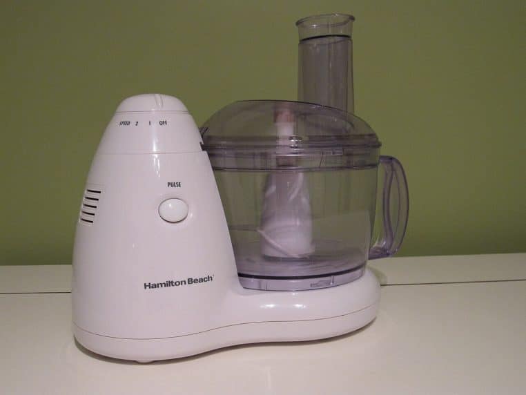Robot culinaire Hamilton Beach avec bol transparent et couteau, installé sur un plan de travail, prêt à hacher légumes et noix.